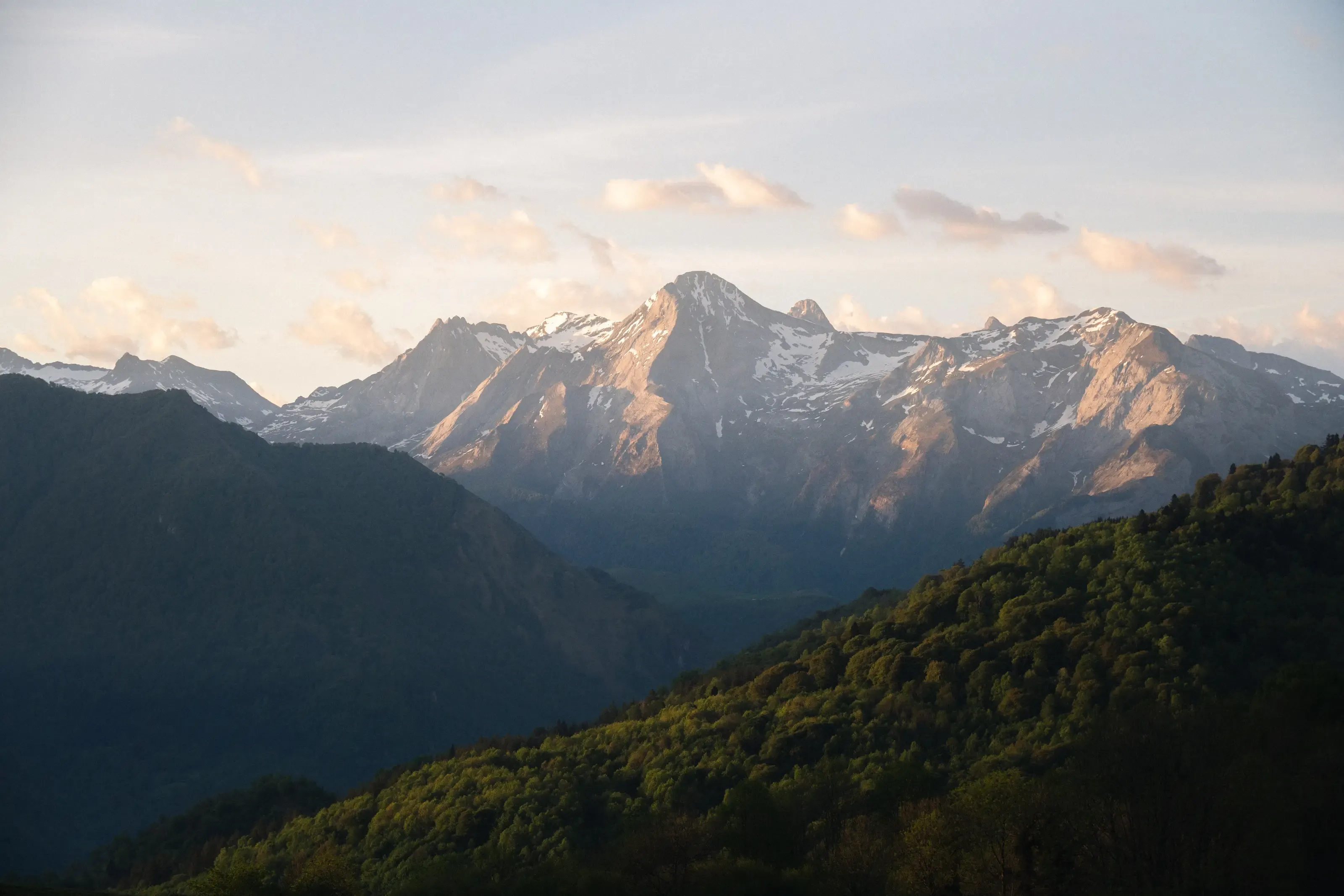 De hauts sommets rocheux parsemés de neige captent la lumière dorée du soleil au-dessus de versants boisés.